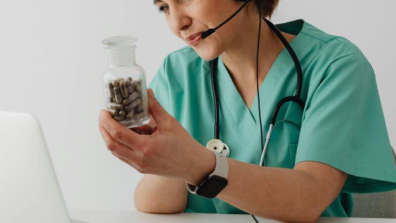A healthcare worker in green scrubs discusses medication during a video consultation.