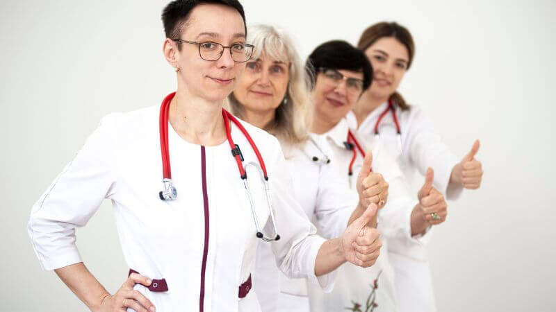 A group of female doctors in white coats showing thumbs up,.