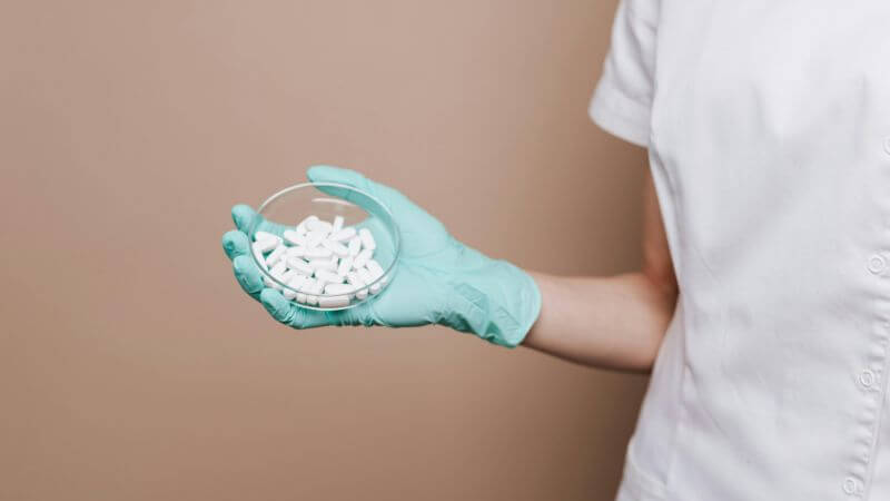 A medical professional in gloves holding a petri dish containing white tablets.