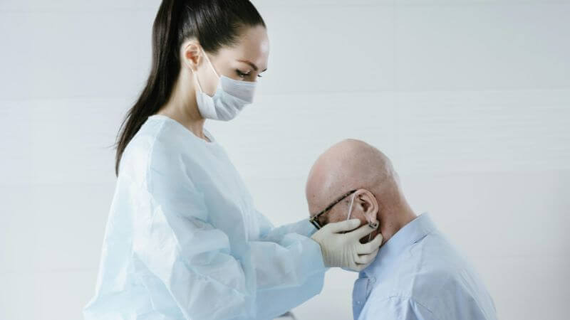 Masked doctor examines elderly patient in clinical setting,