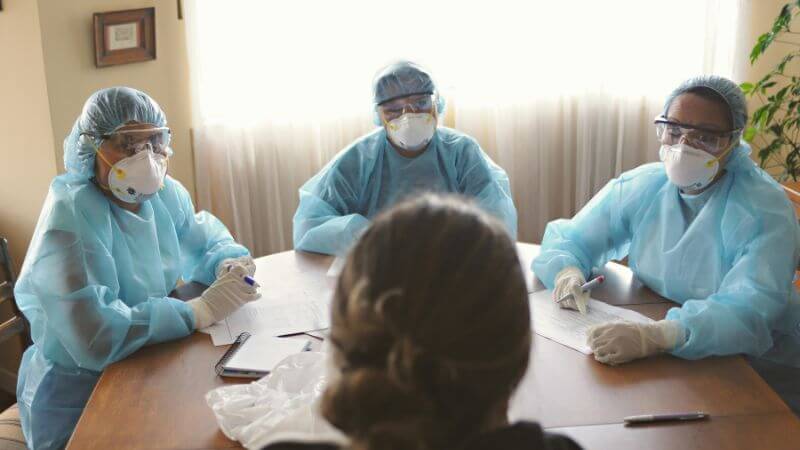 Healthcare workers in masks and gowns discussing patient care.