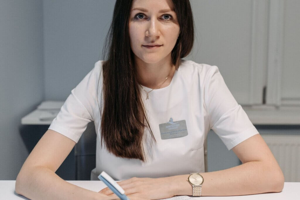 A woman in a white uniform writing in a notebook at an indoor office setting.