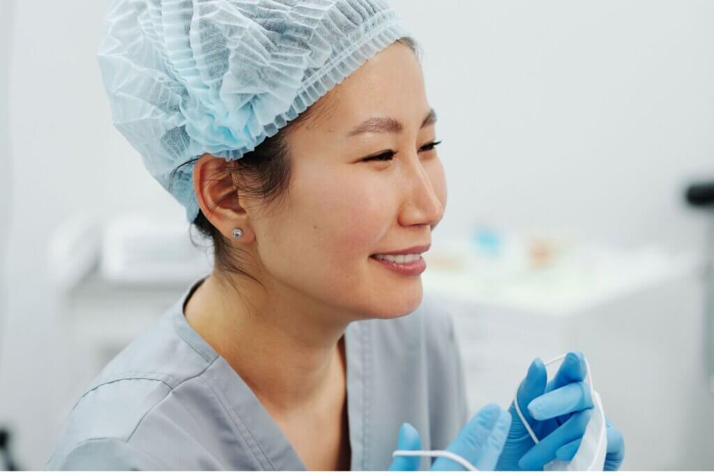 Asian female doctor in scrubs and PPE smiling during a break in a medical clinic