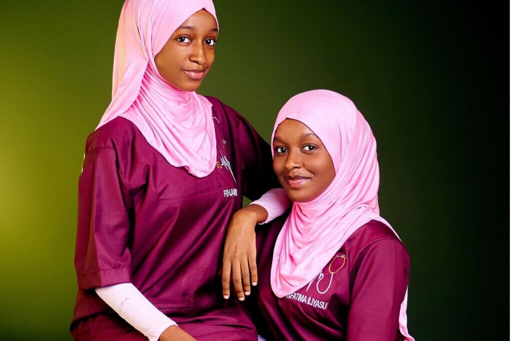 Two nurses in matching burgundy uniforms and hijabs